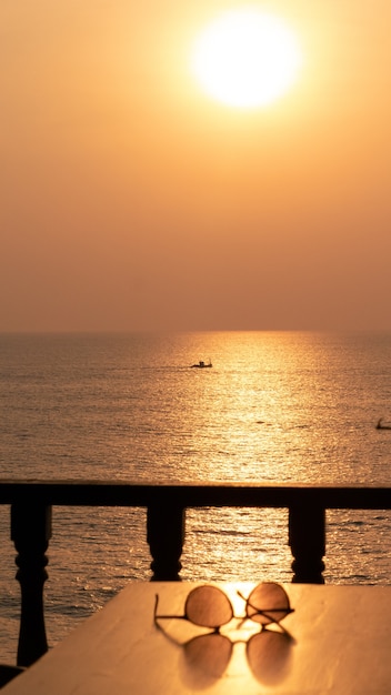 Paar Sonnenbrillen auf dem Tisch am Meer während des Sonnenuntergangs