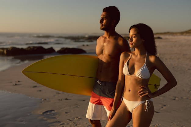 Paar stehen zusammen mit Surfbrett am Strand