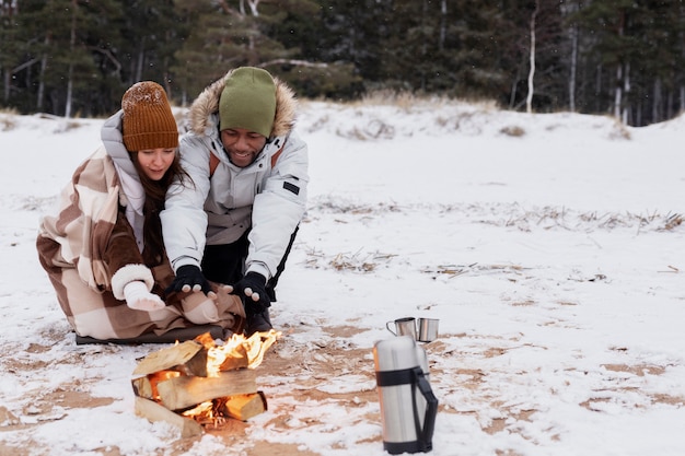 Paar wärmt sich während eines Winter-Roadtrips neben dem Feuer am Strand auf