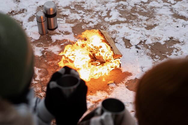 Kostenloses Foto paar wärmt sich während eines winter-roadtrips neben dem feuer am strand auf