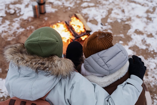 Paar wärmt sich während eines Winter-Roadtrips neben dem Feuer am Strand auf