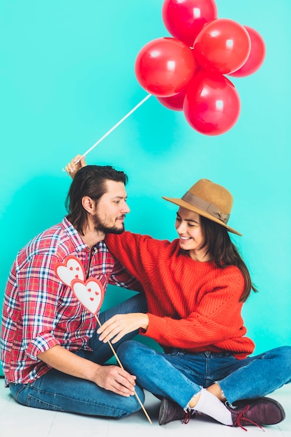 Kostenloses Foto paare, die auf boden mit ballonen und herzen auf stock sitzen