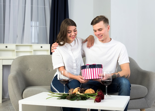 Paare, die auf Couch mit Geschenkbox sitzen