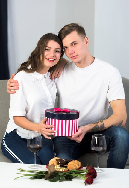 Paare, die auf Couch mit großer Geschenkbox sitzen