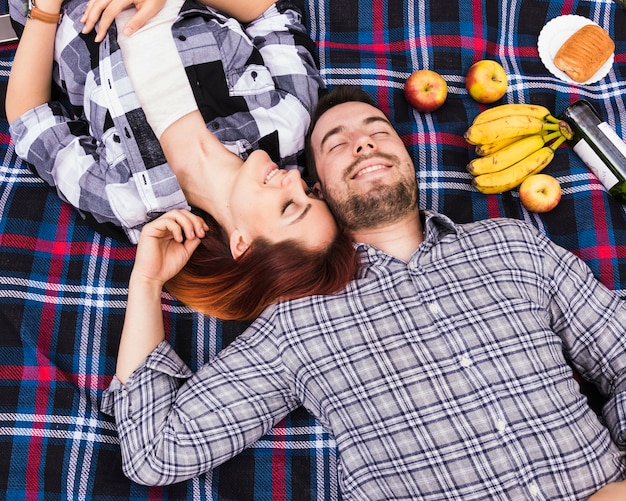 Paare, die auf Decke mit vielen Früchten schlafen; Blätterteig und Champagnerflasche