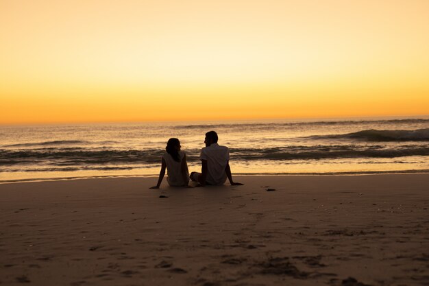 Paare, die auf den Strand während des Sonnenuntergangs aufeinander einwirken