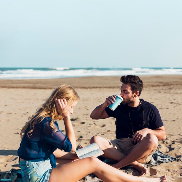 Paare, die auf Strand trinken und lesen