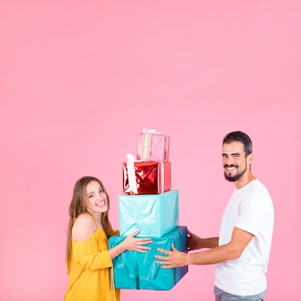 Paare, die bunte geschenkboxen gestapelt gegen rosa hintergrund halten