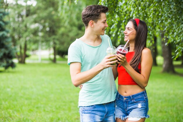 Paare, die einander Röstung von Smoothies im Park betrachten