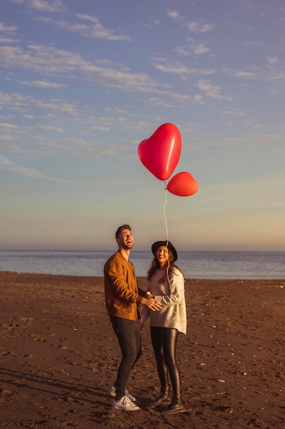 Paare, die Fliegenherzballon auf Seeufer betrachten