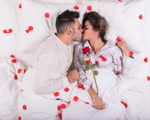 Paare, die im Bett mit den roten rosafarbenen Blumenblättern küssen