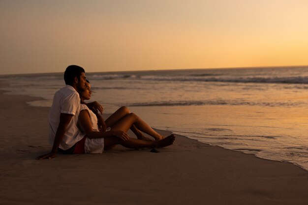 Paare, die Meer auf dem Strand während des Sonnenuntergangs betrachten