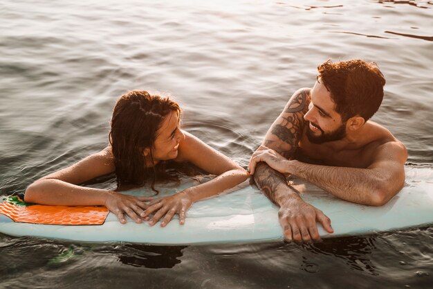 Paare, die mit Surfbrett im Meer stehen