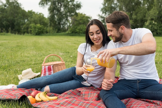 Paare, die Orangensaft auf Picknickdecke essen