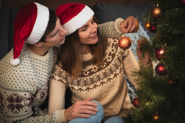 Kostenloses Foto paare, die sankt-hüte verzieren weihnachtsbaum tragen