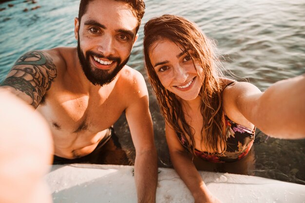 Paare, die selfie im Meer mit Surfbrett nehmen