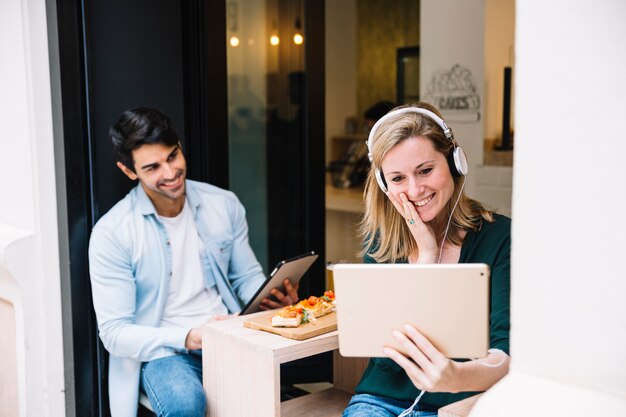 Paare, die Tabletten im Restaurant betrachtend lachen