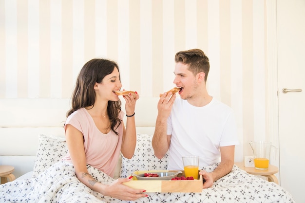 Paare, die Toast auf Bett essen