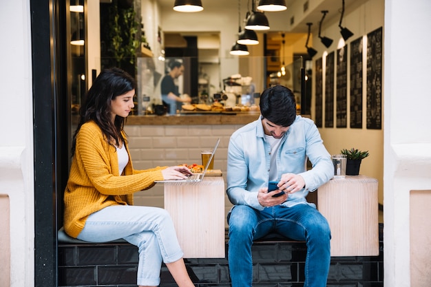 Paare, die zusammen im Café unter Verwendung der Geräte sitzen