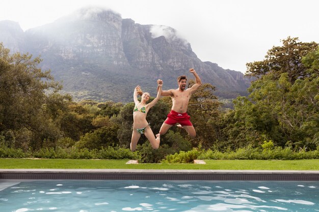 Paare, die zusammen in den Swimmingpool springen