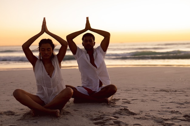 Paare, die zusammen Yoga auf dem Strand durchführen