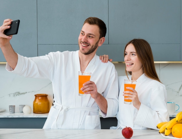 Paare in den Bademänteln, die ein selfie mit Gläsern Saft nehmen