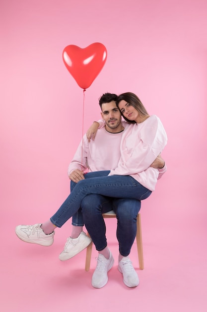 Paare mit dem Herzballon, der auf Stuhl umarmt
