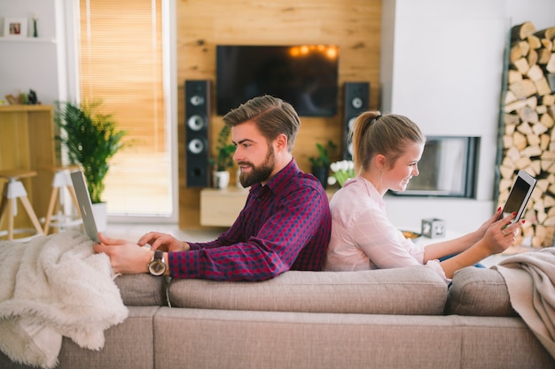 Paare mit den Geräten, die auf Couch sitzen