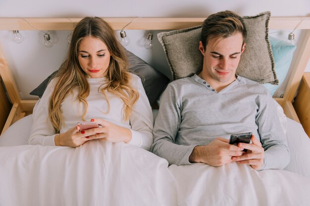 Paare mit den Smartphones, die auf Bett liegen