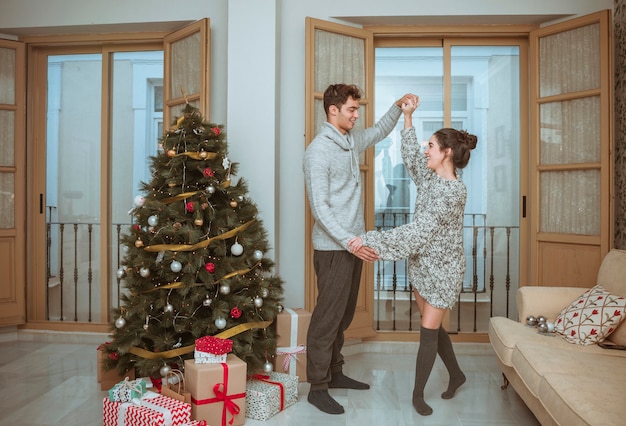 Kostenloses Foto paartanzenholdinghände nähern sich weihnachtsbaum