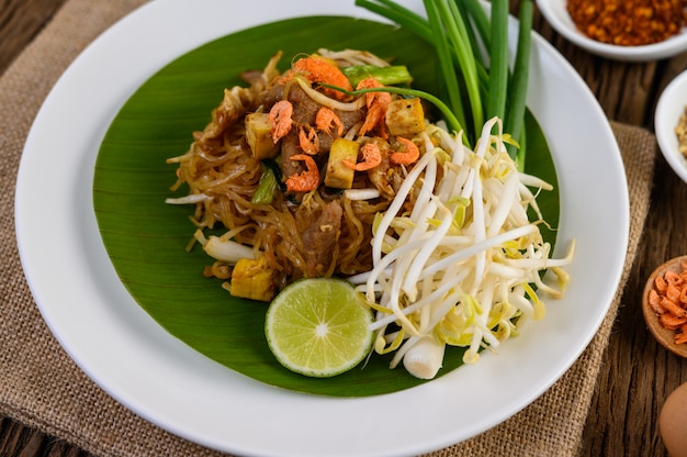 Pad Thai in einem weißen Teller mit Zitrone, Eiern und Gewürzen auf einem Holztisch.