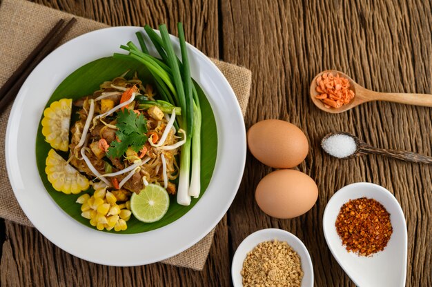 Pad Thai in einem weißen Teller mit Zitrone, Eiern und Gewürzen auf einem Holztisch.