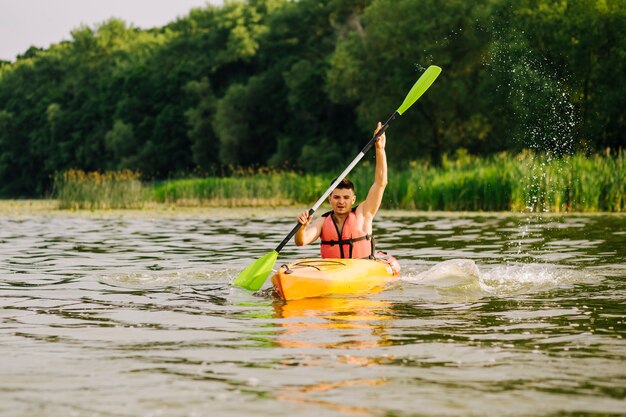 Paddelnkajak des jungen Mannes mit vielen spritzt über dem See