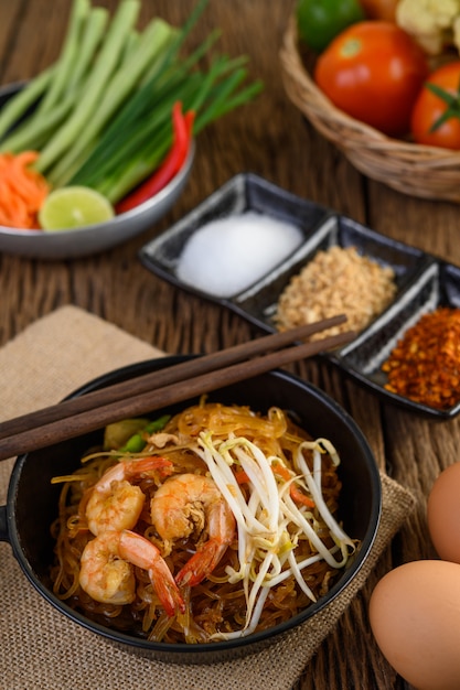 Padthai Garnelen in einer schwarzen Schüssel mit Eiern und Gewürzen auf Holztisch.