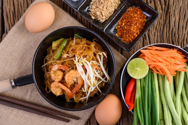 Padthai Garnelen in einer schwarzen Schüssel mit Eiern und Gewürzen auf Holztisch.