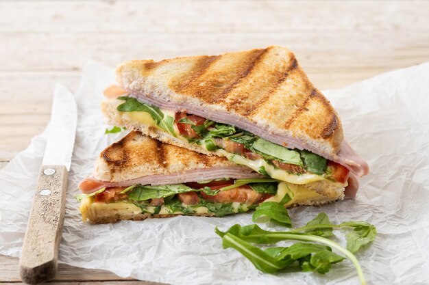 Panini-Sandwich mit Schinken-Käse-Tomate und Rucola auf Holztisch