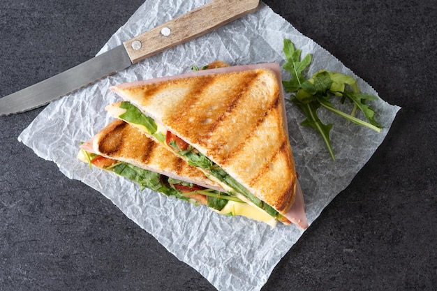 Panini-Sandwich mit Schinken-Käse-Tomate und Rucola auf schwarzem Schieferhintergrund