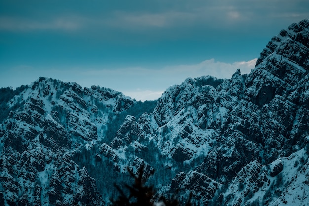 Kostenloses Foto panoramaaufnahme von schneebedeckten gezackten berggipfeln unter bewölktem blauem himmel