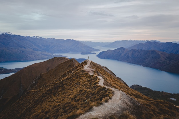 Panoramablick auf den Roys Peak in Neuseeland mit Bergen in der Ferne unter einer hellen Wolkenlandschaft