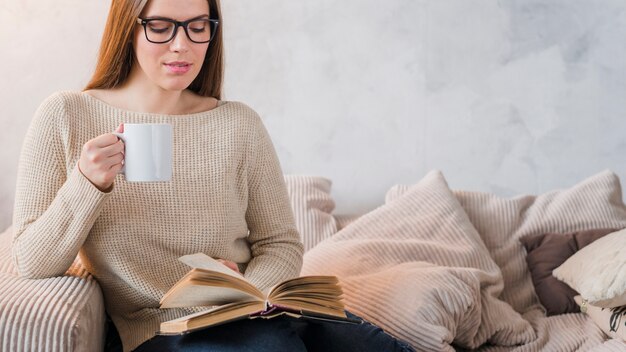 Panoramablick der jungen Frau sitzend auf Sofalesebuch