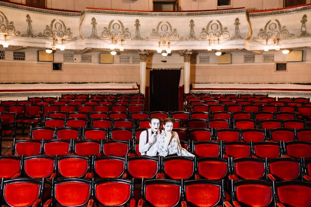 Pantomimepaarkünstler, der zusammen auf Stuhl im Auditorium sitzt