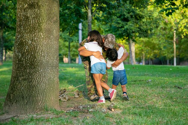 Papa trifft sich mit zwei Kindern nach der militärischen Missionsreise und umarmt Kinder auf Gras im Park.