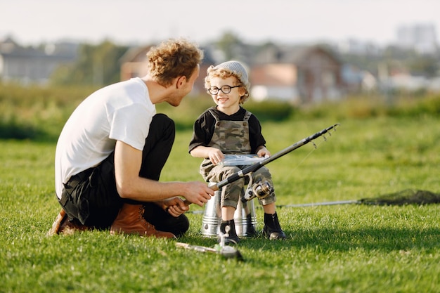 Kostenloses Foto papa und sein kleiner junge verbringen gemeinsam zeit im freien. gelockter kleinkindjunge, der einen khakifarbenen overall trägt. junge sitzt auf einem eimer und hört seinem vater zu