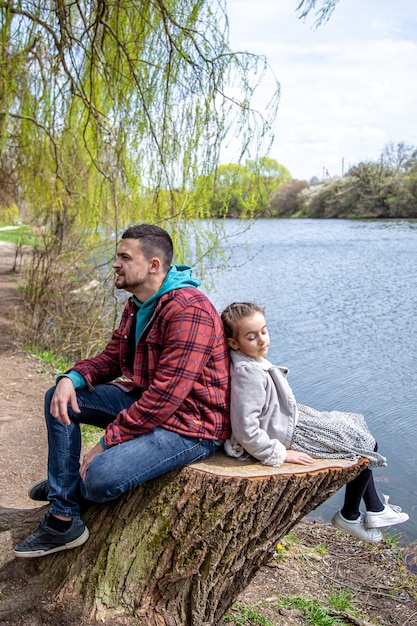 Papa und seine kleine Tochter sitzen im zeitigen Frühjahr im Wald am Fluss und genießen die Natur.