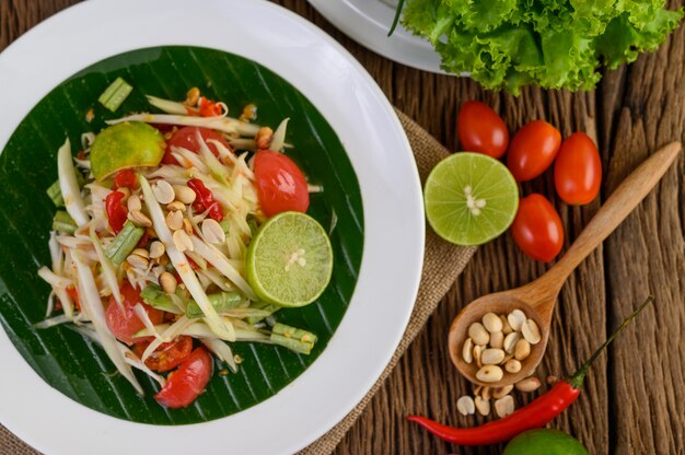 Papayasalat (Som tum Thai) auf einem weißen Teller auf einem Holztisch.