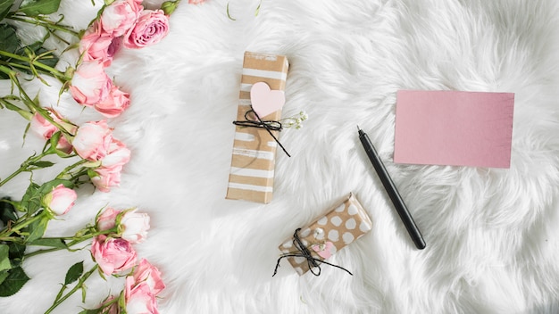 Papier in der Nähe von Stift, Geschenken und frischen Blumen auf Wolldecke