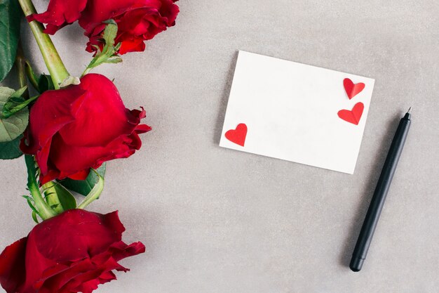 Papier mit kleinen Herzen in der Nähe von Stift und Blumen