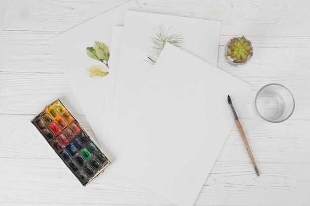 Papiere mit Pflanzenfarben in der Nähe von Glas, Pinsel und Wasserfarben