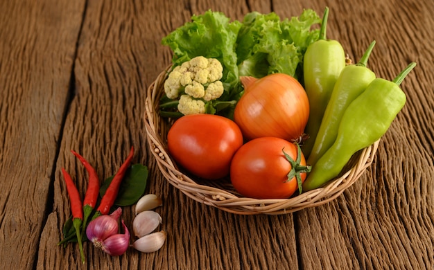 Paprika, Tomate, Zwiebel, Salat, Chili, Schalotte, Knoblauch, Blumenkohl und Kaffirlimettenblätter auf einem Holzkorb auf Holztisch
