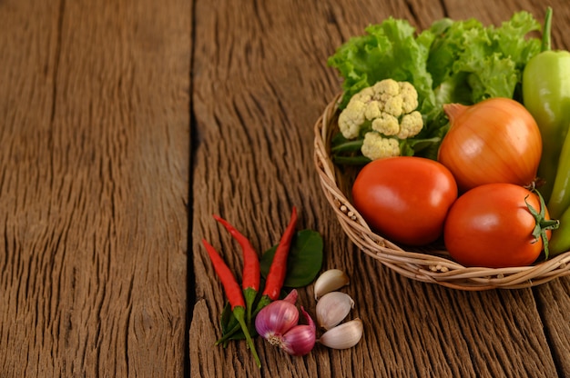 Paprika, Tomate, Zwiebel, Salat, Chili, Schalotte, Knoblauch, Blumenkohl und Kaffirlimettenblätter auf einem Holzkorb auf Holztisch